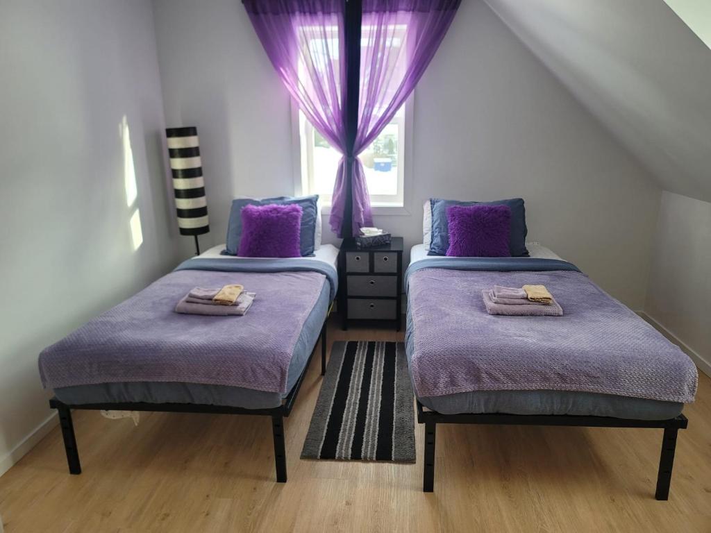 a bedroom with two beds with purple sheets and a window at Cute apartment close to highway in Edmundston