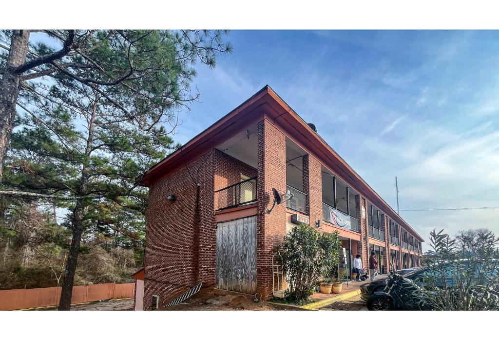 a red brick building with a porch and trees at Studio 6 Suites Albany, GA in Albany