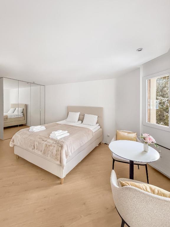 a white bedroom with a large bed and a table at Wasserfall - Zentrum - Balkon - Seeblick - Küche in St. Moritz