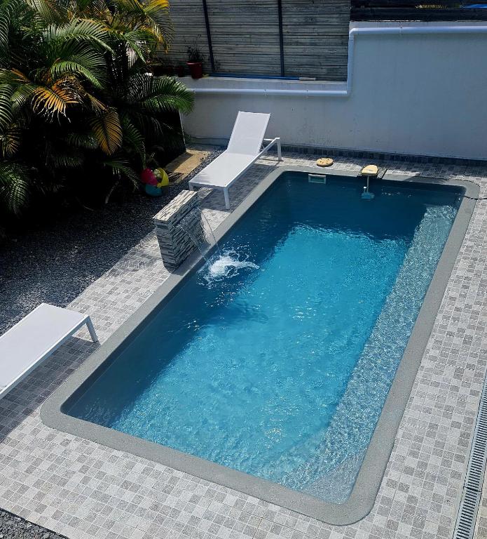 a swimming pool with two white chairs and a swimming pool at Les Caramboles- Appartement Cosy in Sainte-Suzanne