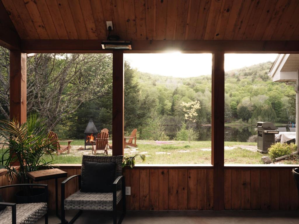 a screened porch with a large window looking out at a yard at Chalet rustique, Lac paisible, Canot, Famille in La Conception