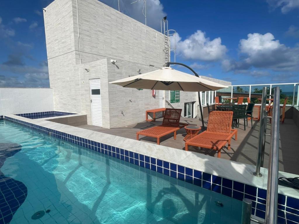 a swimming pool with a patio with an umbrella and chairs at MAKARANDUBA BEACH 304 - Piscinas Naturais e Coração de Porto in Porto De Galinhas