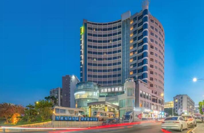 a tall building with cars parked in front of it at Shenzhen Xingwei Yifeng Hotel in Shenzhen