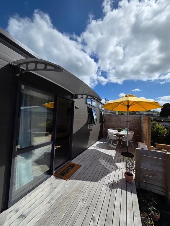 a deck with a table and an umbrella at Puriri Tiny Home in Orewa