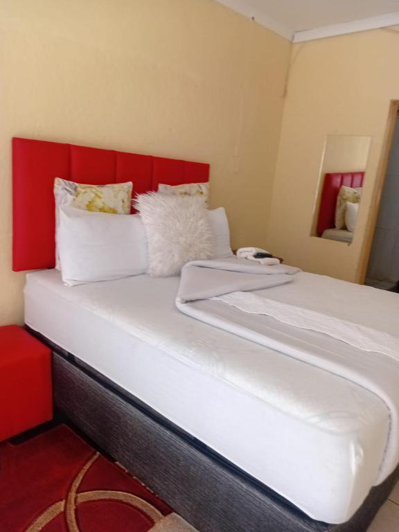 a bed with a red headboard and white pillows at Happy Guest House in Mahikeng