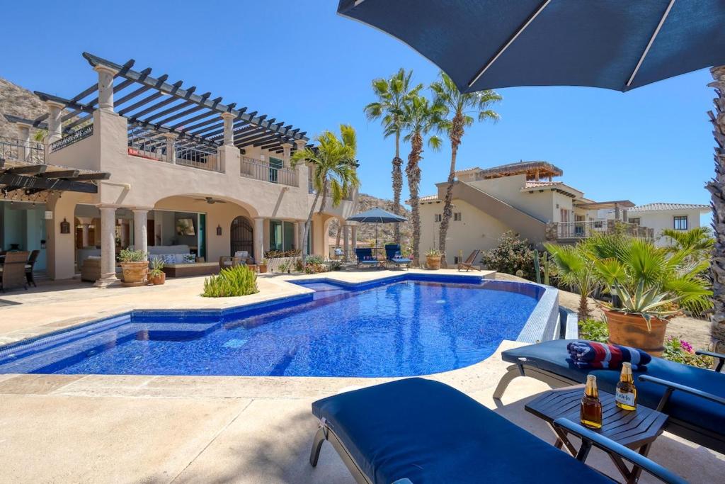 a pool with chairs and an umbrella next to a house at The Fairway Villa in San José del Cabo
