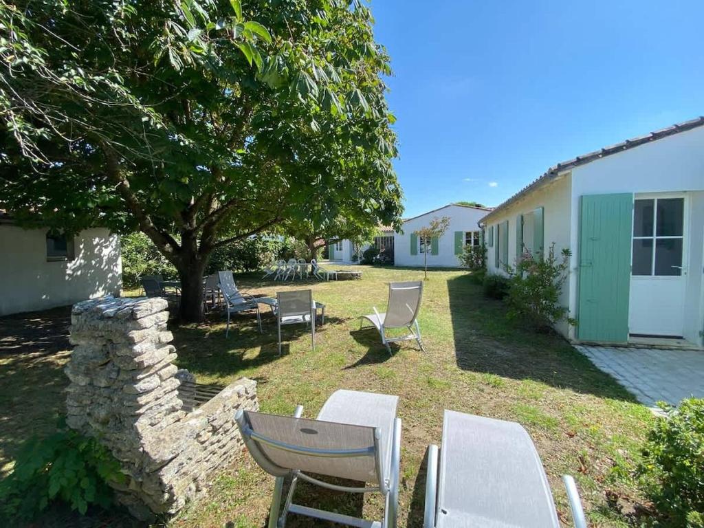 a yard with chairs and a table and a tree at La Villa du Clocher in Saint-Clément-des-Baleines