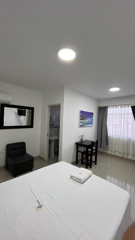 a bedroom with a white bed and a black chair at Hostal Bali - Talara in Talara