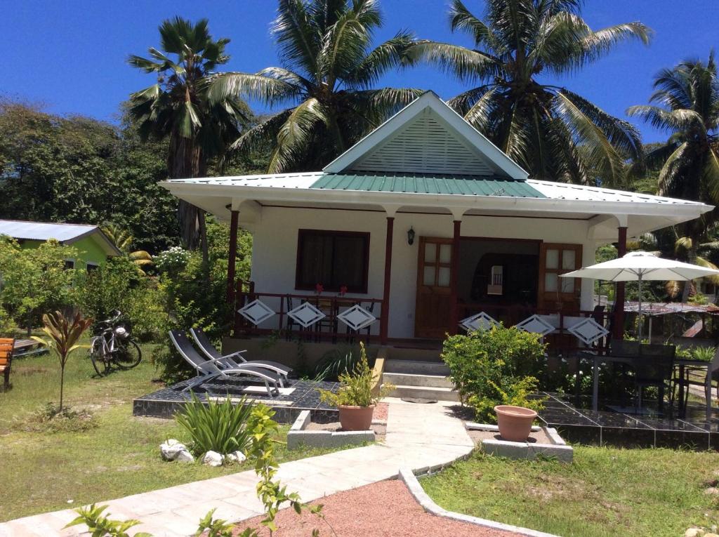 une petite maison blanche avec des palmiers en arrière-plan dans l'établissement Agnes Cottage - Emerald, à La Digue