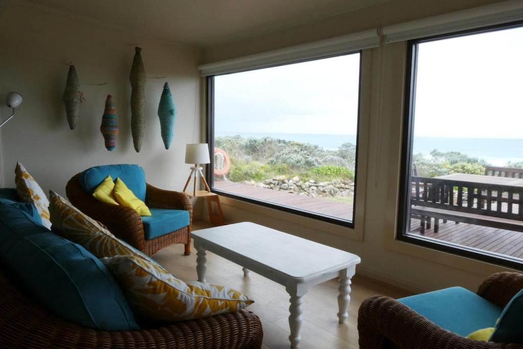 a living room with two chairs and a table and windows at Absolute beach front stunning views day and night in Cape Bridgewater