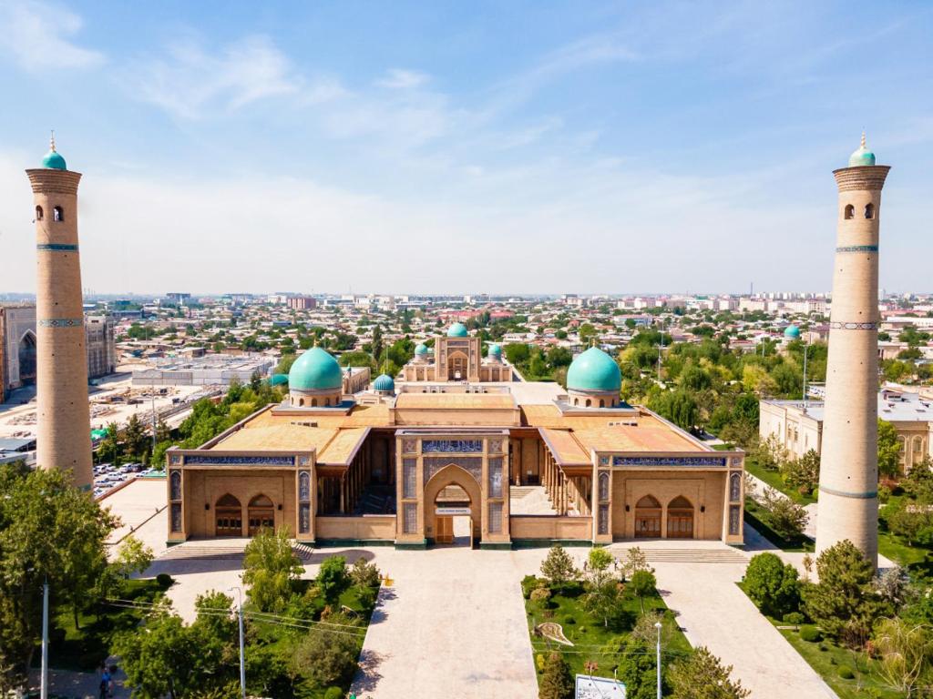 a mosque with two domes and a city in the background at JONIKA Sleep & Go Inn in Aktepa-Chigatay