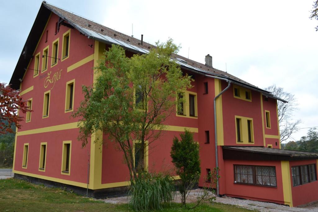 a red and yellow building with a tree in front at Penzion Zoja in Rudník
