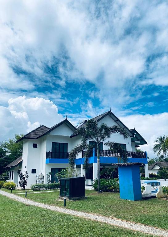 a white house with blue balconies and palm trees at Villa Alaya Malai in Setiu