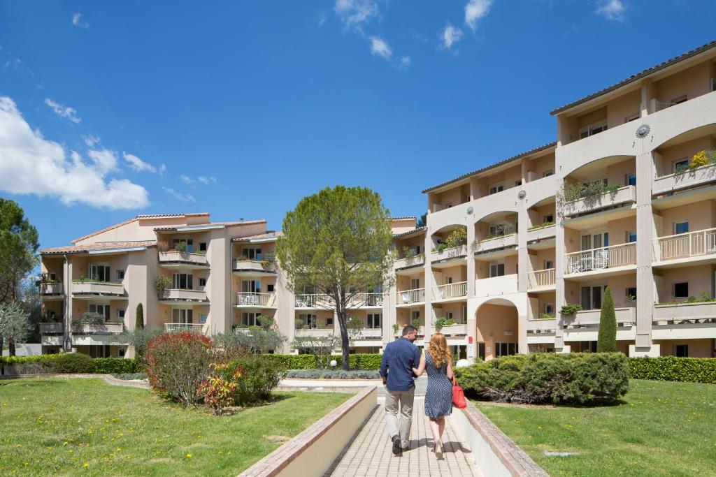 Un uomo e una donna in piedi davanti a un palazzo di Résidence les Grands Pins a Gréoux-les-Bains