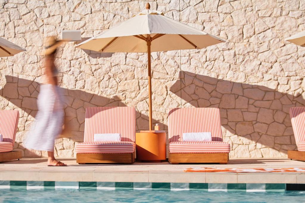 a person is standing near a pool with chairs and an umbrella at The Lodge Wadjemup in Rottnest Island