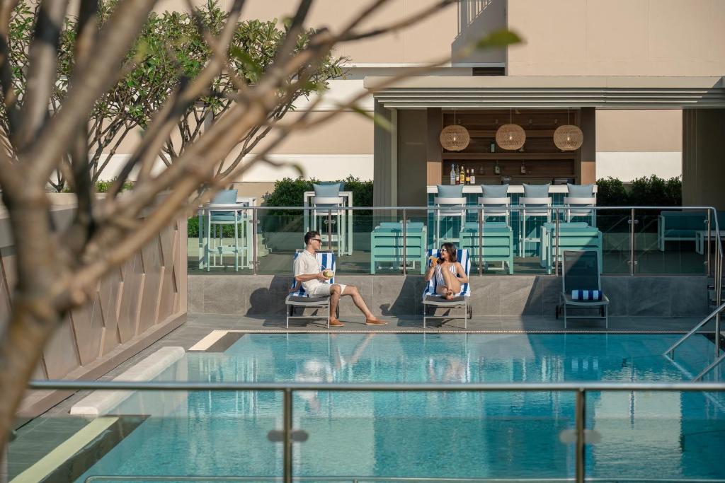 two people sitting in chairs next to a swimming pool at Hyatt Place Bangkok Sukhumvit 1 in Bangkok