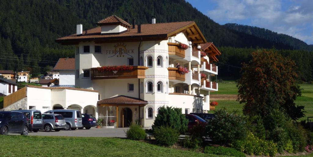 een groot wit gebouw met auto's geparkeerd op een parkeerplaats bij Hotel Fernblick in San Valentino alla Muta