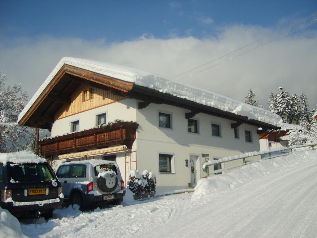 dom z dwoma samochodami zaparkowanymi na śniegu w obiekcie Pension Feichter w mieście Söll