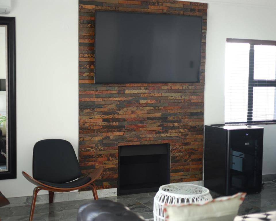 a living room with a brick fireplace with a flat screen tv at His Grace Eagles Guesthouse in Bloemfontein