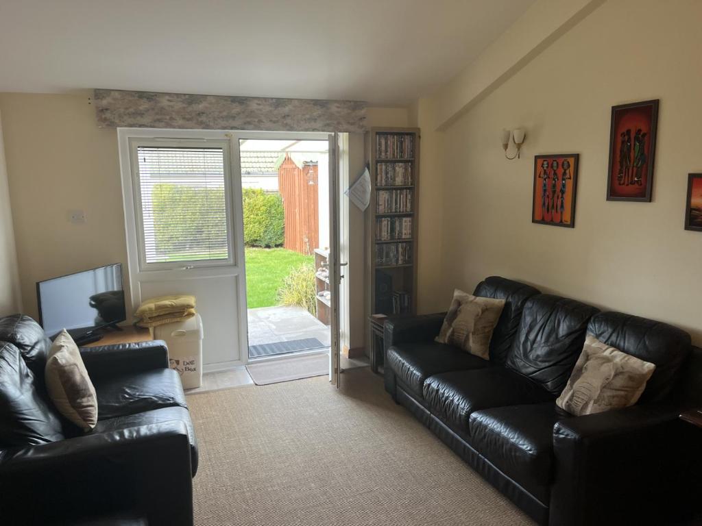 a living room with black leather couches and a sliding glass door at Hopeman Cottage in Hopeman
