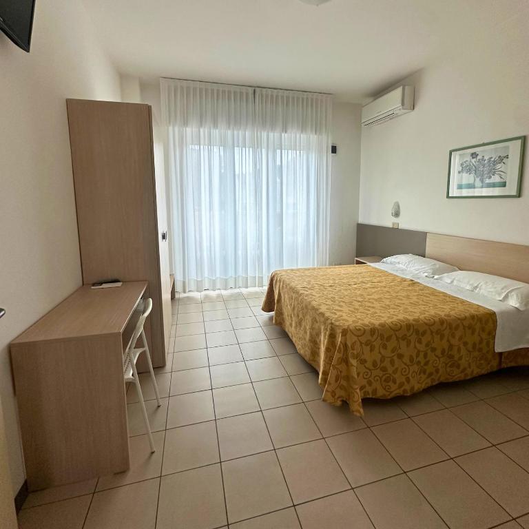 a bedroom with a bed and a desk and a window at Hotel Furga B&B in Cervia