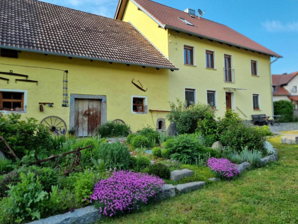a garden in front of a yellow house with purple flowers at Ferienwohnung Schindler in Nittenau