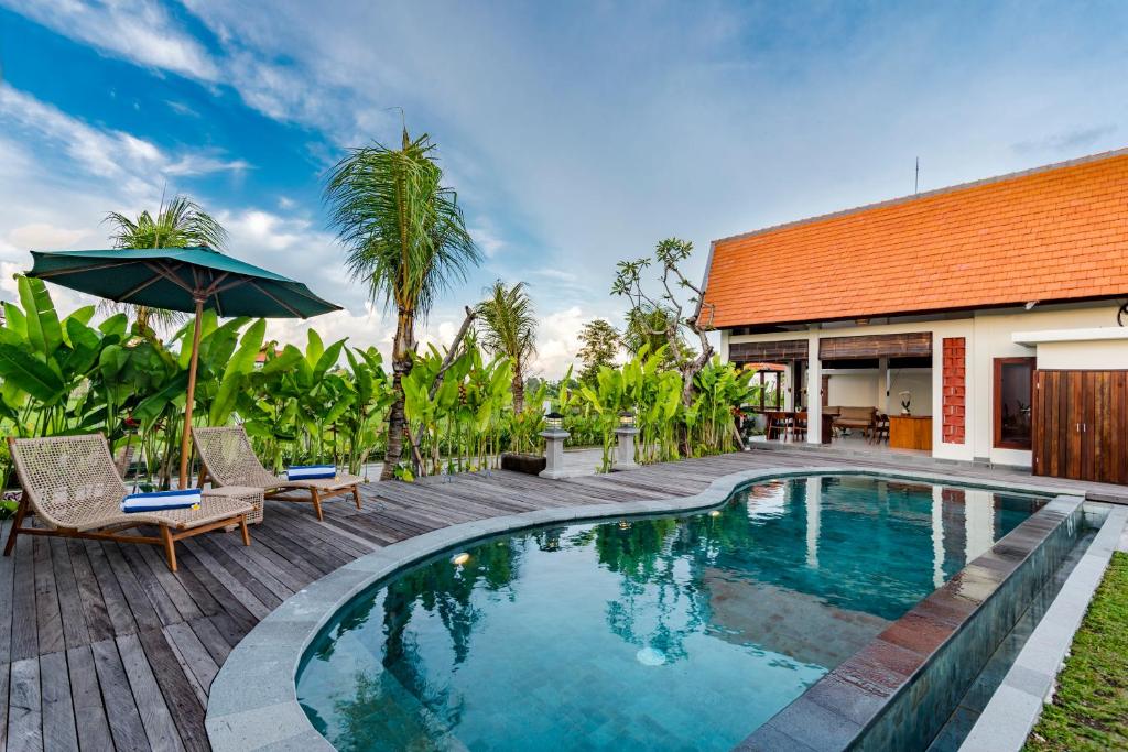 a pool with chairs and an umbrella next to a house at Svadarma Bali Villa by Dhananjaya Hospitality in Darmasaba