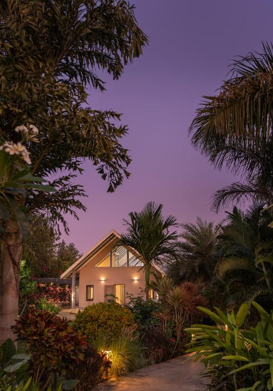 a home at night with palm trees in the foreground at SaffronStays Eden - 3BR vineyard-side pool villa with jacuzzi, farm dining, stargazing deck & lawns for celebrations in Nashik