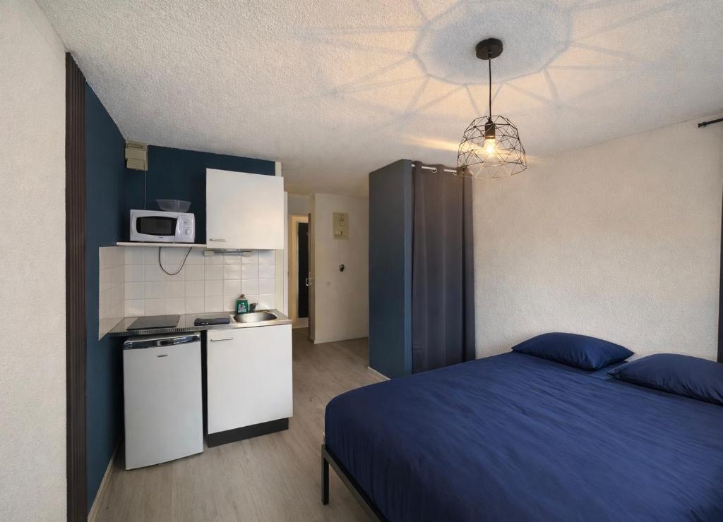 a bedroom with a blue bed and a kitchen at Les Logis de Paray - app 124 in Paray-le-Monial