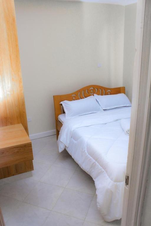 a bedroom with a bed with white sheets and pillows at Aurora Loisse Suites in Nakuru