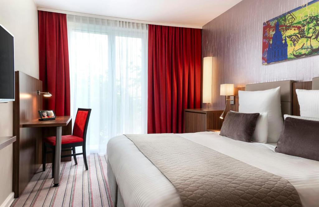 a hotel room with a bed and a desk and red curtains at Leonardo Hotel Dresden Altstadt in Dresden