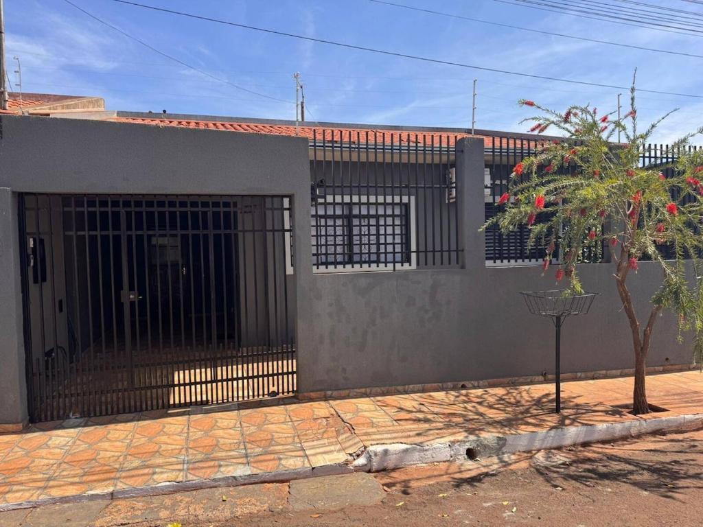 a building with a gate and a tree in front of it at Casa espaçosa com ar em todos os quartos in Ourinhos