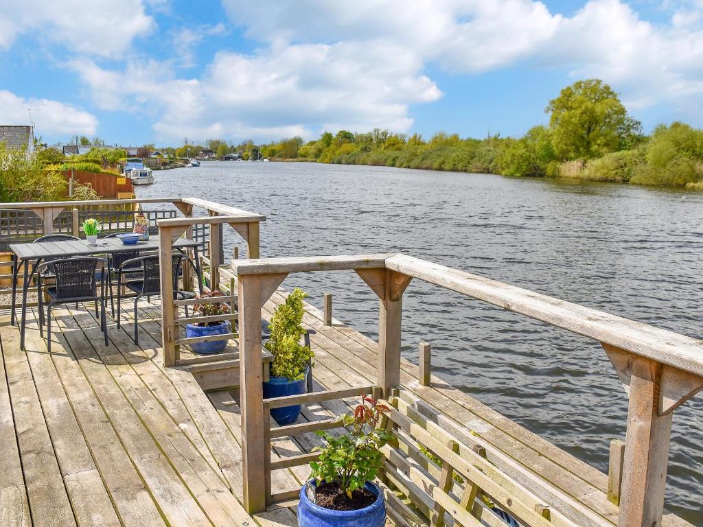 a wooden dock with a table and chairs on a river at Evening Glory in Brundall
