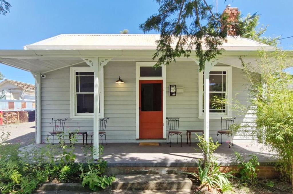 a white house with a red door and chairs at A Warm & Charming Retreat in Castlemaine