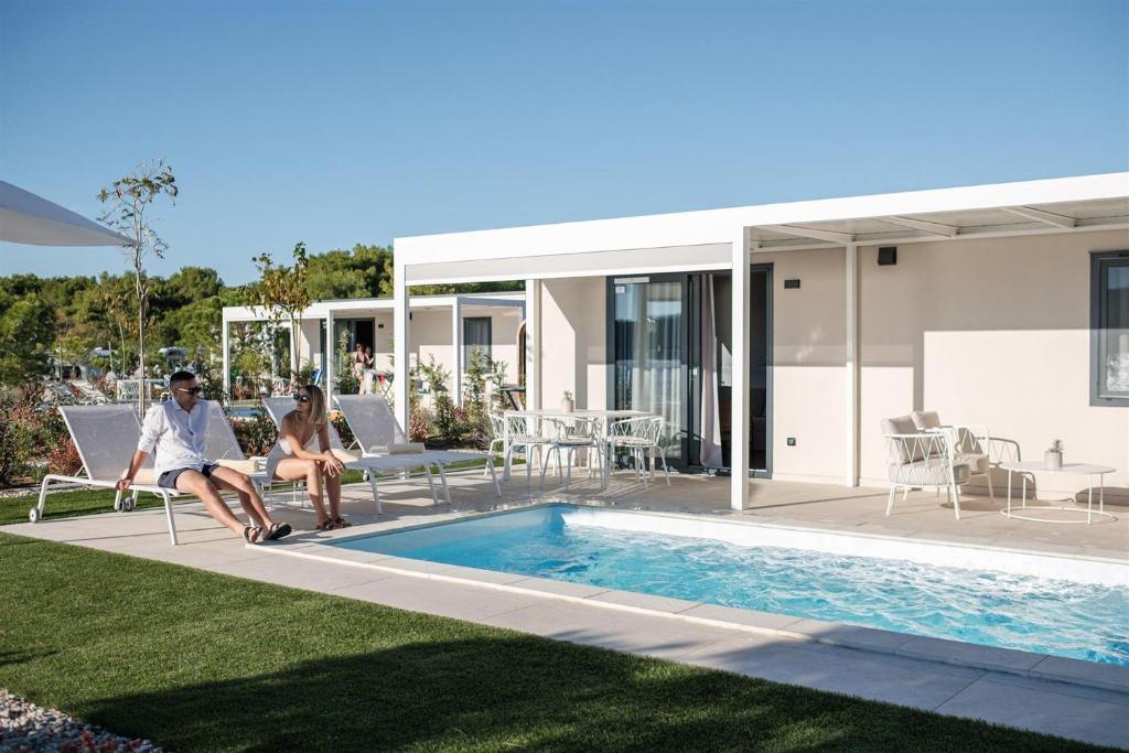two people sitting on chairs next to a swimming pool at Amadria Exclusive Beach Villa in Šibenik