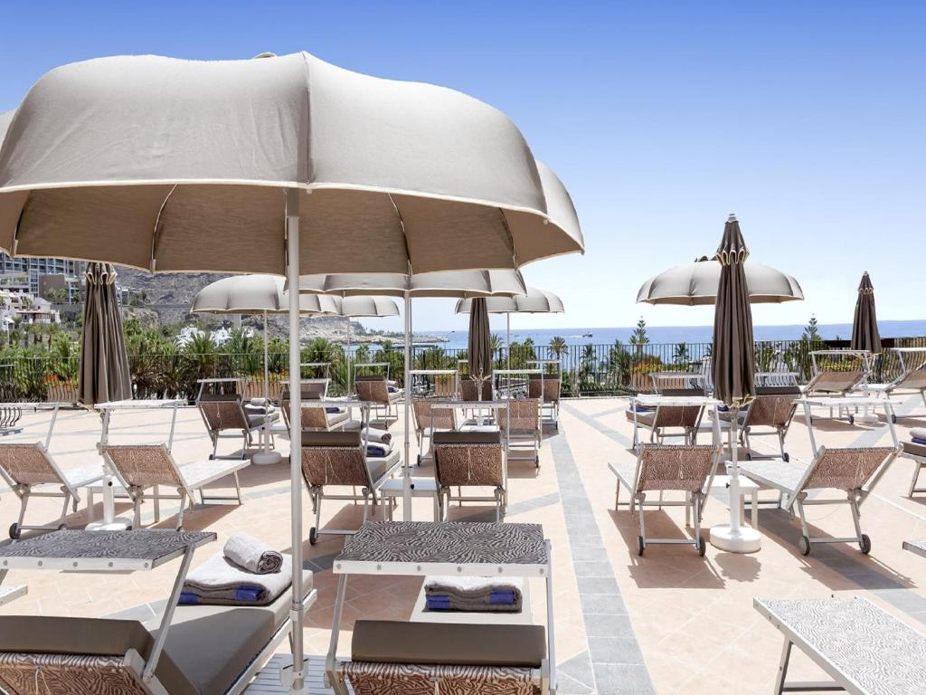 un patio con sillas, mesas y sombrillas en Idyll Suites - Adults Only en Playa del Cura
