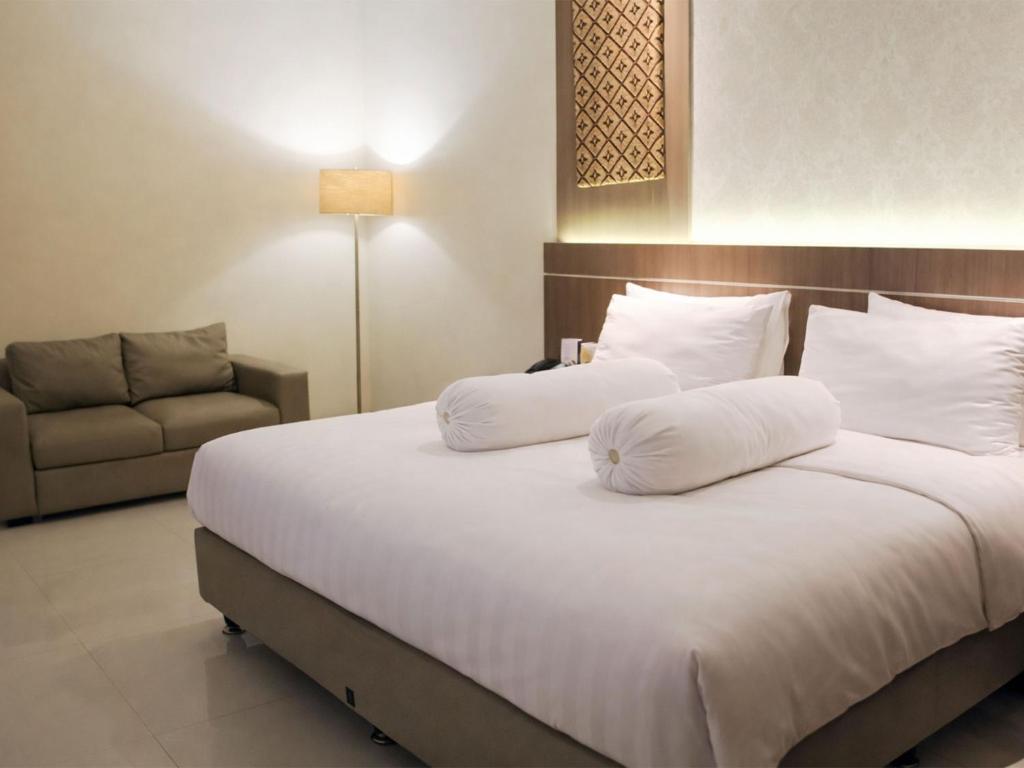 a bedroom with a bed with white pillows and a couch at Nevada Ketapang Hotel in Ketapang