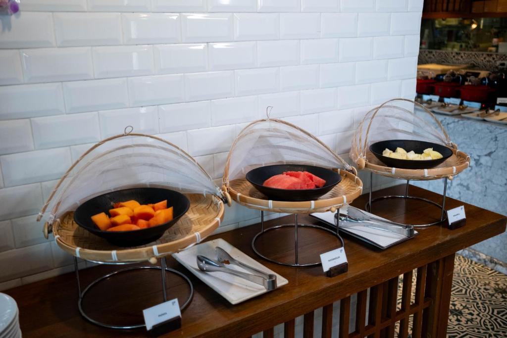 A fruit station with individual bowls of cut melon and pineapple under wicker covers.