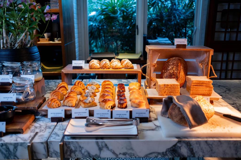 A bakery-style breakfast counter with pastries, sliced bread, and serving utensils.
