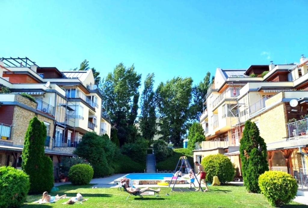 a group of people sitting in the grass in front of buildings at Koczor Apartman in Balatonfüred