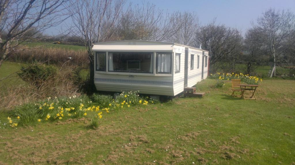 mała przyczepa siedząca na polu z kwiatami w obiekcie Caravan by Sea w mieście Morfa Nefyn