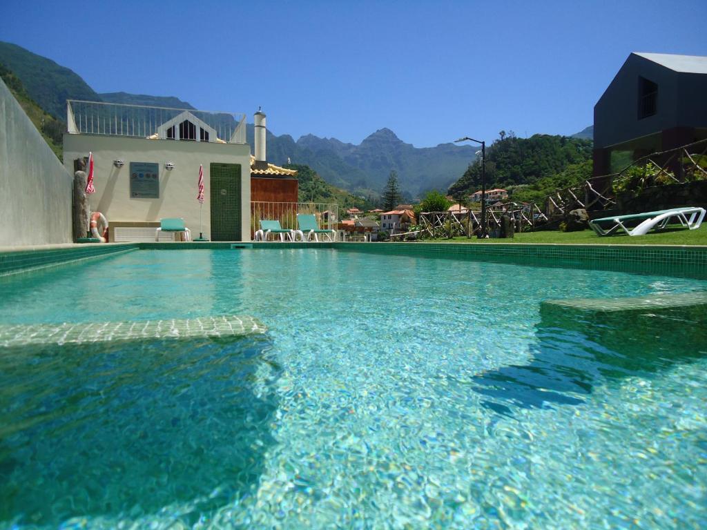 a swimming pool with blue water in front of a house at A Casa Estrelícia-Dourada Garcês in São Vicente