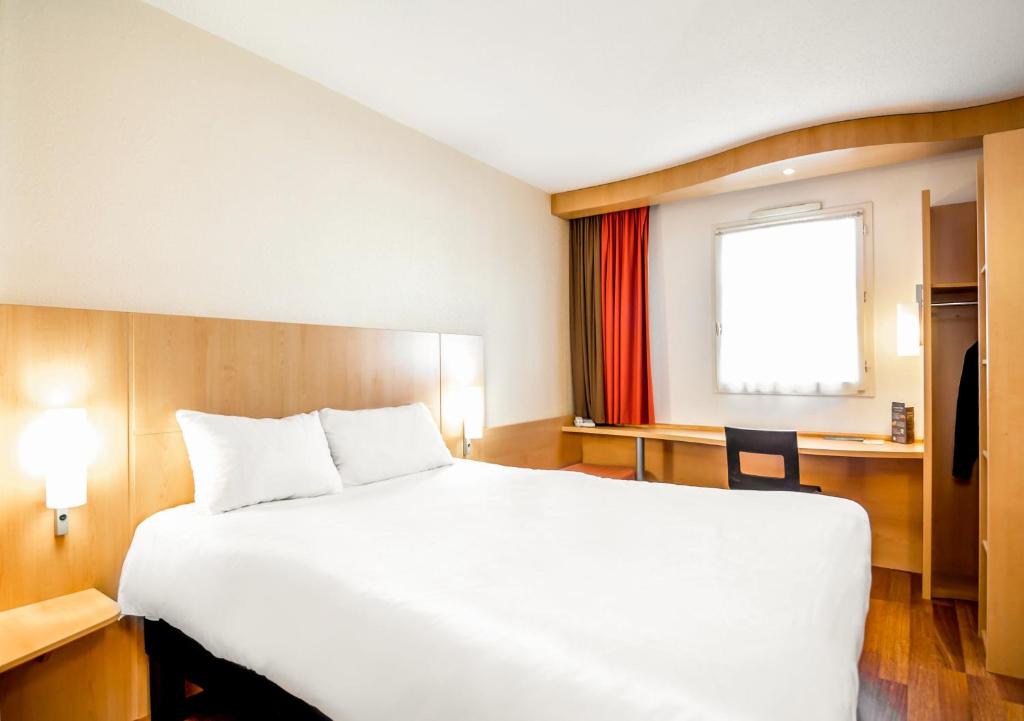 a hotel room with a bed, desk, and a lamp at Ibis Ripollet in Ripollet