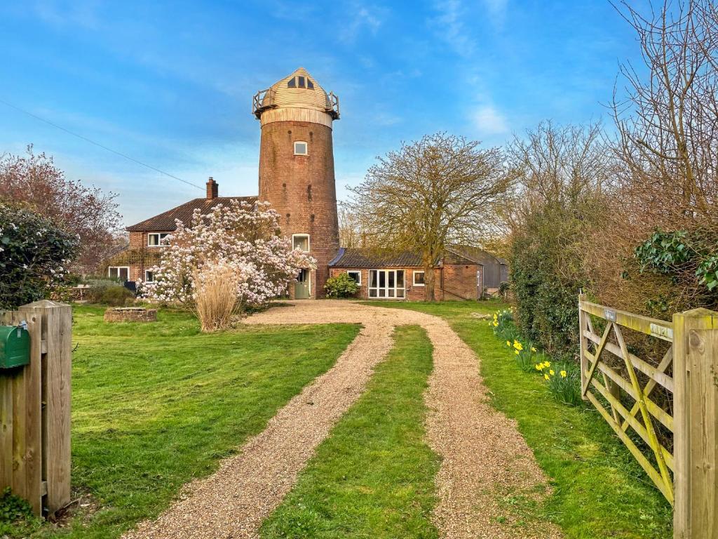 a house with a tower on top of a dirt road at Finest Retreats - The Old Windmill in Hindolveston