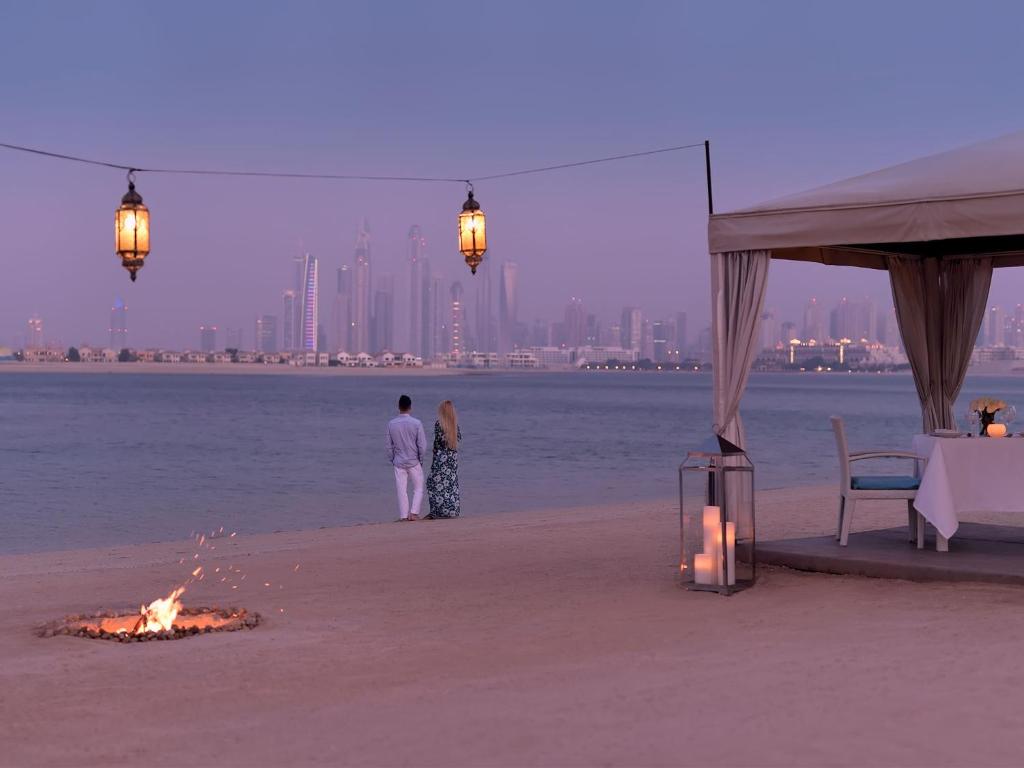 a couple standing on the beach with a fire on the beach at Kempinski Hotel Palm Jumeirah in Dubai