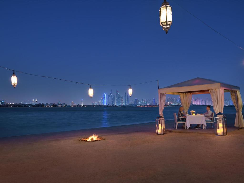 a couple sitting under a gazebo on the beach at night at Kempinski Hotel Palm Jumeirah in Dubai