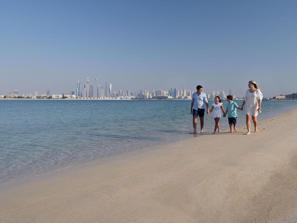 a family walking on the beach near the water at Kempinski Hotel Palm Jumeirah in Dubai