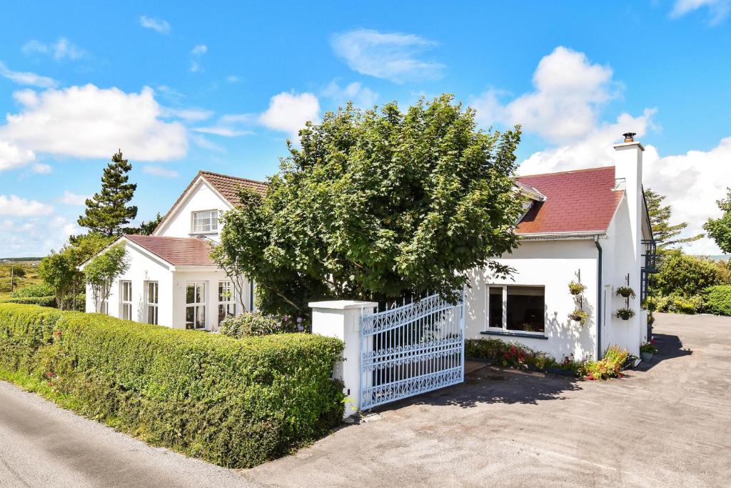 a white house with a white fence and a tree at Mannin Lodge in Ballyconneely