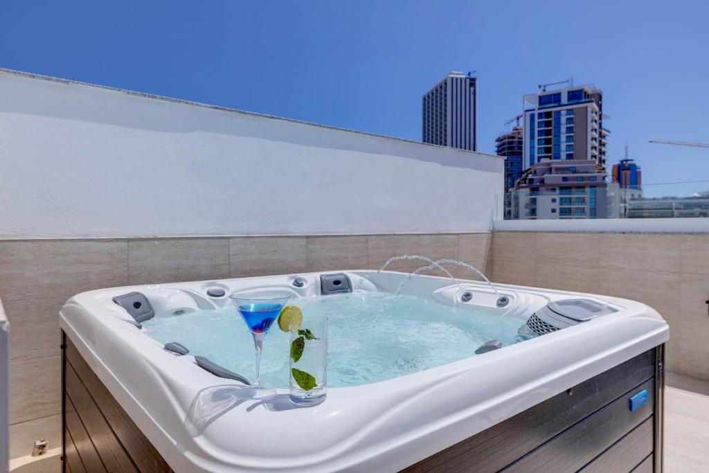 a hot tub on a roof with a drink in it at Bayside A Apartments in St. Julianʼs