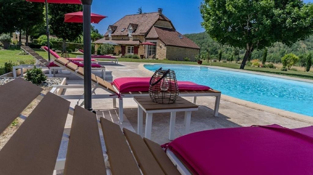 a pool with benches and umbrellas next to a house at Ancienne grange rénovée avec piscine in Vaillac